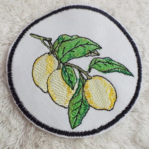 May include: Embroidered patch featuring a branch of lemons with green leaves. The lemons are yellow with a white outline. The patch is circular and has a black border.