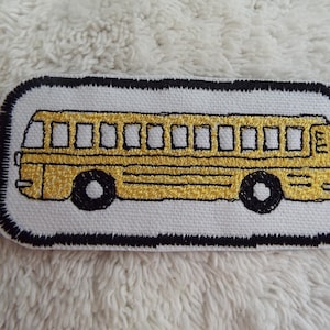 Może przedstawiać: Haftowana naszywka przedstawiająca żółty autobus szkolny z czarnymi kołami i konturami. Naszywka ma białe tło i czarną obwódkę. Odpowiednia do kurtek, plecaków lub innych materiałowych przedmiotów.