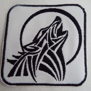 May include: Square patch with a black and white design. The patch features a howling wolf silhouette in front of a full moon. The wolf and moon are black, and the background is white. The patch has a black border.