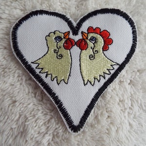 May include: Embroidered heart-shaped patch with two yellow chickens facing each other. The chickens have red combs and wattles. The patch has a black outline.