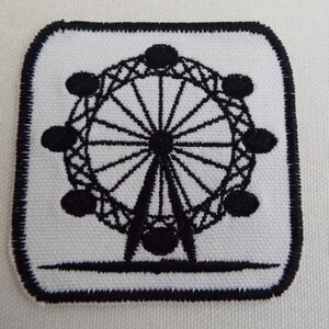 May include: Embroidered patch featuring a black and white design of a Ferris wheel. The patch has a white background with a black border and a black Ferris wheel design in the center. The patch is square with rounded corners.