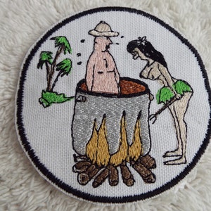 May include: Embroidered patch with a cartoon image of a person in a pot over a fire with another person standing nearby. The pot is brown and gray, the fire is orange and yellow, and the people are pink and white.
