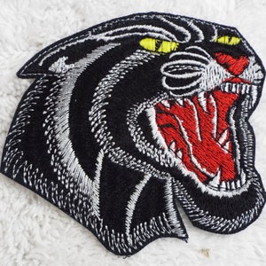 May include: Embroidered iron-on patch of a black panther with a white outline and red open mouth, with yellow eyes.