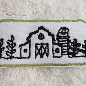 May include: A white embroidered patch with a black outline of a farmhouse, silo, and trees. The patch has a green border.