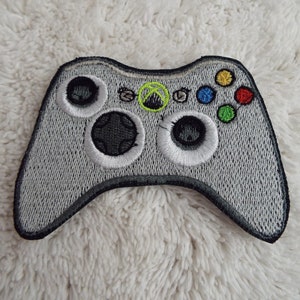 Op de afbeelding: Een witte geborduurde patch van een videogamecontroller. De controller heeft een groen Xbox-logo, zwarte knoppen en een witte rand.