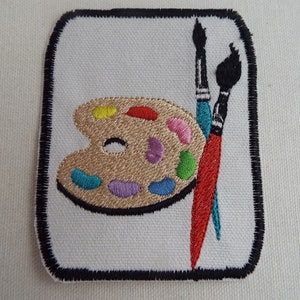 May include: A white embroidered patch with a black border, featuring a brown and gold paint palette with colorful paint wells and two red and blue paintbrushes.
