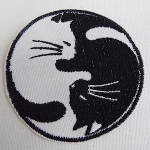 May include: Black and white embroidered patch of two cats facing each other in a yin yang design.