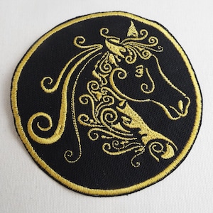 May include: A round black patch with a gold embroidered design of a horse's head with intricate swirls and curls.