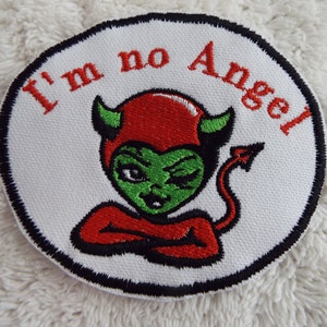 May include: A white, round embroidered patch with a black border. The patch features a red devil with green skin and a black tail. The text "I'm no Angel" is embroidered in red on the patch.