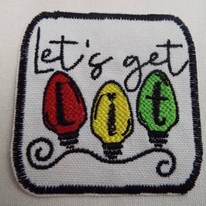 May include: White embroidered patch with black stitching. The patch features three light bulbs in red, yellow, and green with the text "Let's get lit" above them.