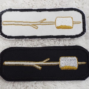 May include: Two embroidered patches, one white and one black, with a gold stick figure holding a white marshmallow on a stick.