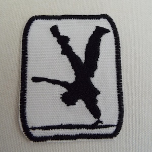 Puede incluir: Parche bordado en blanco y negro de una persona haciendo una parada de manos. El parche es rectangular y tiene un borde negro.