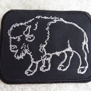 May include: A black embroidered patch with a white outline of a bison. The patch is rectangular and has a stitched border.