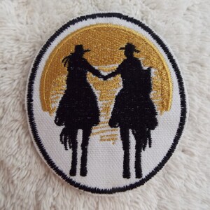 May include: Embroidered patch featuring two silhouettes of people riding horses, facing each other, against a gold sunset background. The patch is circular and has a white background with a black outline.