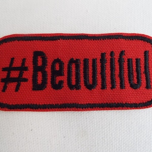 Puede incluir: Parche de tela rectangular rojo con texto bordado en negro que dice "#Beautiful".