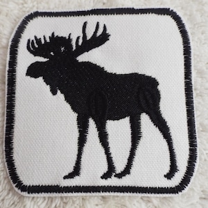 以下が含まれることがあります： 白い背景に黒い縁取りで、黒い刺繍のヘラジカのシルエットパッチ