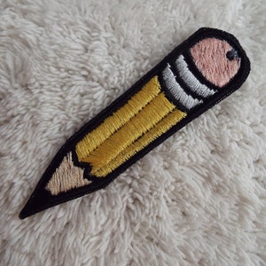 May include: A yellow and black embroidered pencil patch. The pencil has a pink eraser and a white stripe.