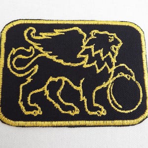 May include: A black embroidered patch with a gold outline of a winged lion holding a ball.