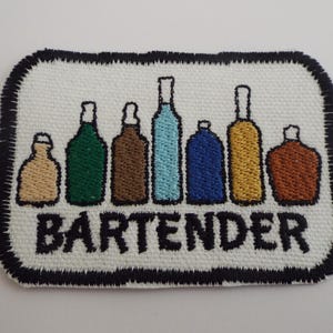 May include: Embroidered patch featuring a row of colorful bottles with the word "BARTENDER" in black text. The patch has a white background with a black border, perfect for jackets, bags, or other fabric items.