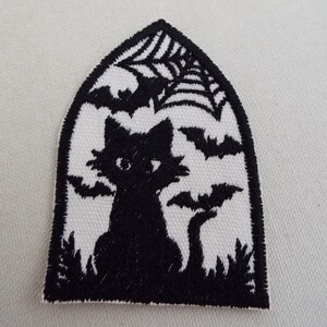 May include: Black and white Halloween patch featuring a black cat silhouette, bats, and a spider web design. The patch is in a gothic arch shape, perfect for adding a spooky touch to clothing or accessories.