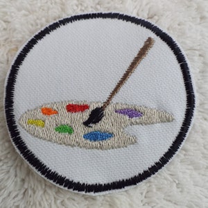 May include: A white embroidered patch with a black border, featuring a paint palette with colourful paint and a paintbrush.