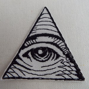 May include: Black and white embroidered patch of an eye inside a triangle. The eye is detailed with eyelashes and a pupil.