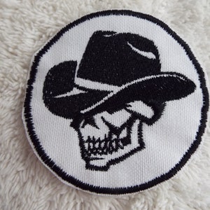 May include: A white embroidered patch with a black skull wearing a cowboy hat. The patch is circular and has a black outline.