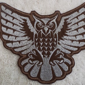 May include: Brown embroidered iron-on patch of an owl with outstretched wings. The owl is outlined in white thread and has a detailed design.