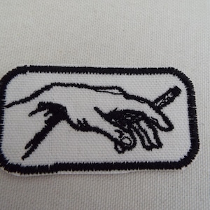 Peut inclure: Patch brodé noir et blanc d'une main tenant un stylo, sur fond blanc et bordure noire.