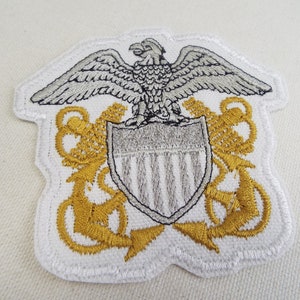 May include: White embroidered patch with a silver eagle, shield with stripes, and two gold anchors.
