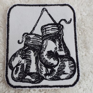 May include: A white embroidered patch with a black outline depicting two boxing gloves hanging from a hook.