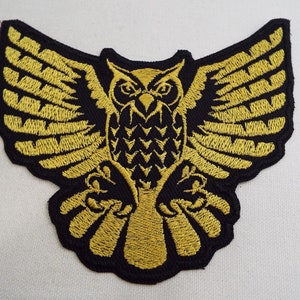 May include: Gold embroidered iron-on patch of an owl with its wings spread out.
