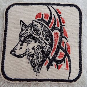 Puede incluir: Parche bordado en blanco y negro de una cabeza de lobo con un diseño tribal rojo y negro detrás.