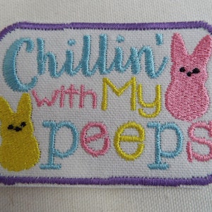 May include: Embroidered patch with the phrase "Chillin' with My Peeps" in blue, pink, and yellow lettering. The patch features cartoon bunny figures in yellow and pink. The patch has a white background with a purple border.