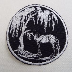 Könnte beinhalten: Ein gestickter Aufnäher in Schwarzweiß, der ein Pferd zeigt, das unter einer Trauerweide steht.