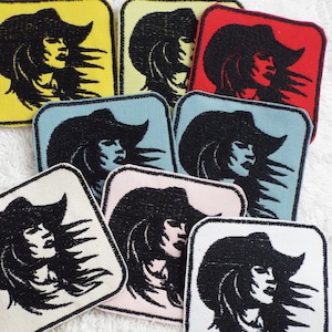 May include: A set of nine iron-on patches featuring a black and white silhouette of a woman wearing a cowboy hat. The patches are in various colors, including yellow, red, blue, and pink.