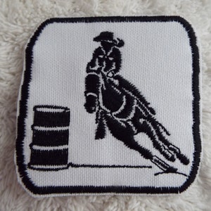 May include: Black and white embroidered patch of a person riding a horse around a barrel. The patch is on a white background.