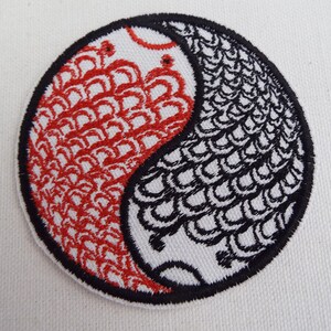Könnte beinhalten: Ein schwarzes und rotes gesticktes Yin-Yang-Symbol mit einem schuppigen Muster. Das Yin-Yang-Symbol ist ein kreisförmiges Design mit zwei Hälften, eine schwarz und eine rot, die gegensätzliche Kräfte im Gleichgewicht darstellen.
