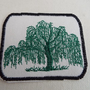 May include: Embroidered patch featuring a green weeping willow tree on a white background. The tree has a detailed design with cascading branches and a textured trunk. The patch is rectangular with rounded corners and a black border.