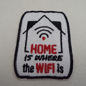 Puede incluir: Parche bordado con fondo blanco y borde negro. El parche presenta un gráfico de casa con un símbolo WiFi y el texto "HOME is where the WIFI is" en rojo y negro.