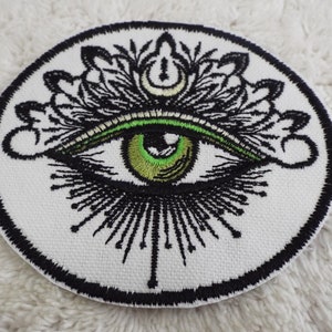 Op de afbeelding: Een witte geborduurde patch met een zwart en groen oog omringd door een zwart mandala-ontwerp.