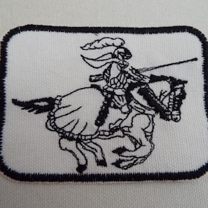 Puede incluir: Parche bordado en blanco y negro de un caballero montando un caballo. El caballero lleva armadura y un casco con una pluma. El caballo se levanta sobre sus patas traseras.