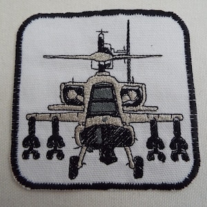 Puede incluir: Parche bordado con una ilustración detallada de un helicóptero militar en tonos grises y negros. El parche tiene un fondo blanco con un borde negro, mostrando el diseño de la aeronave.