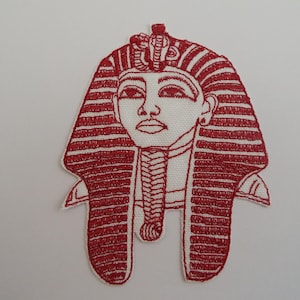 May include: Embroidered patch depicting an Egyptian pharaoh's face in red thread on a white background. The design includes the pharaoh's headdress, face, and collar. This patch is likely intended for decorative use on clothing or accessories.