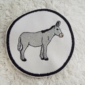 May include: A white embroidered patch with a black outline, featuring a gray donkey standing on a white background.