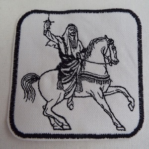 May include: Black and white embroidered patch depicting a person riding a horse. The person is holding a sword in their right hand and is wearing a robe. The horse is rearing up on its hind legs.