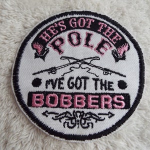 May include: White round embroidered patch with black stitching. The patch says "He's got the pole I've got the bobbers" in pink lettering with a black and white illustration of two fishing rods.