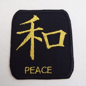 May include: Black fabric patch with gold embroidered Japanese kanji character for peace, "和", and the word "PEACE" below.