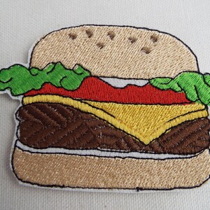 May include: Embroidered patch of a hamburger with a brown patty, yellow cheese, red tomato, green lettuce, and a tan bun.