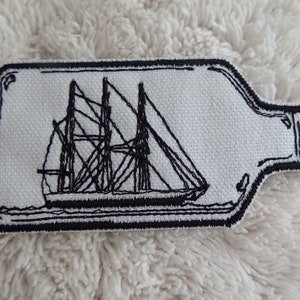 May include: A black and white embroidered patch depicting a ship in a bottle. The patch is on a white background and has a black outline.